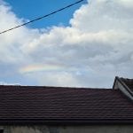 a rainbow above a roof with fluffy white clouds