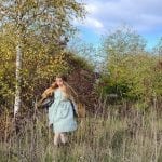 a blonde lady in a mint green dress in some grass with trees