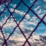 a blue sky and clouds at sunset behind a chain fence