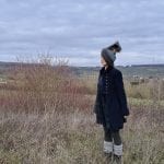 a lady standing outside in a coat with a scarf blown in her face