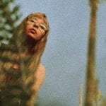 a white blonde lady looking down on some plants, camera is on the ground facing up