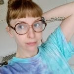 white lady with dark blonde hair in a tye-dye tshirt and tortoiseshell-type framed glasses