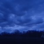 a cloudy blue sky above a dark treeline