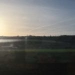 view of a sunrise over a hill from inside a train