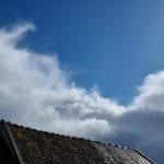 large clouds in a blue sky above a roof