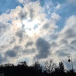 sun behind white clouds in a blue sky