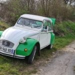 a cute green and white classic little car parked off the side of a dirt road