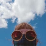 blonde lady wearing face mask and sun glasses with blue sky and white clouds