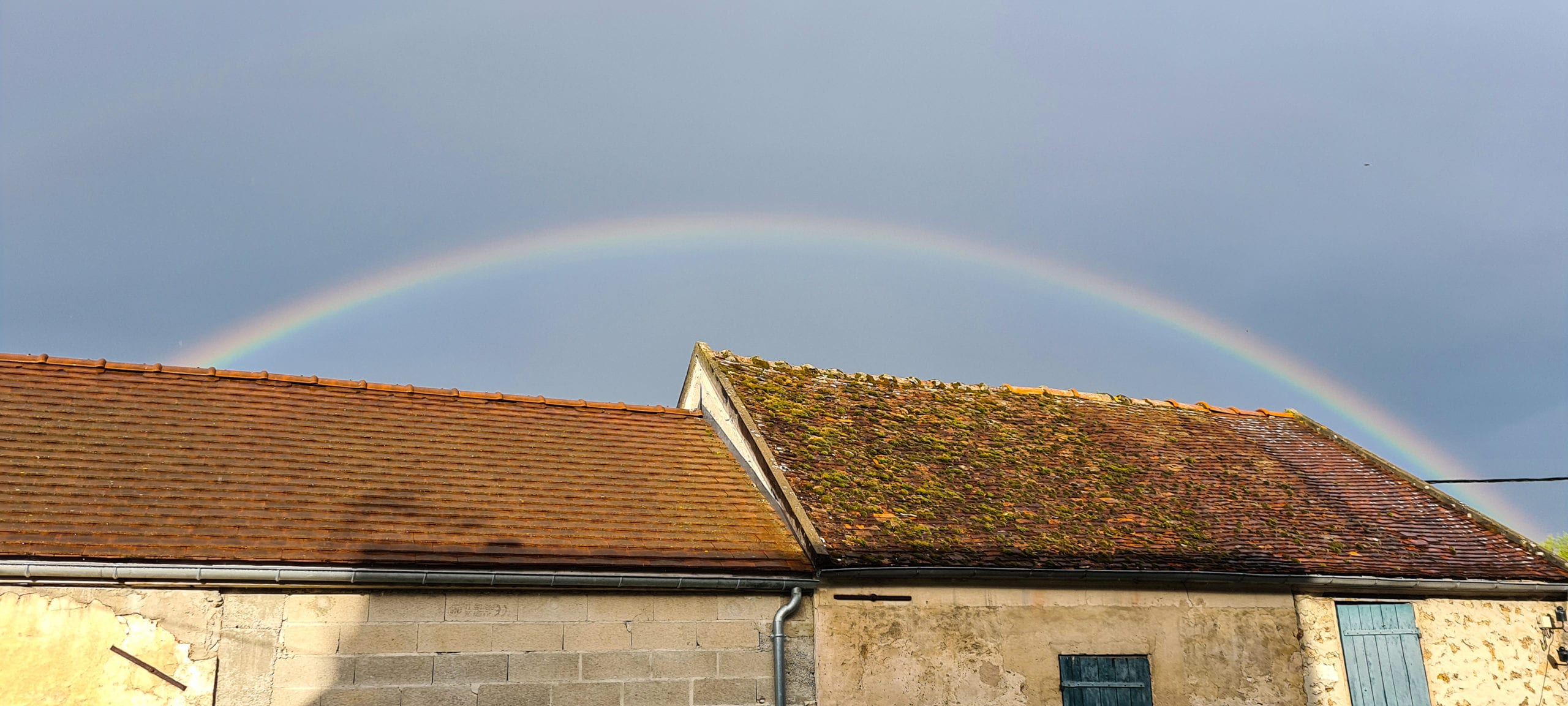 a rainbow in a grey sky above some roofs