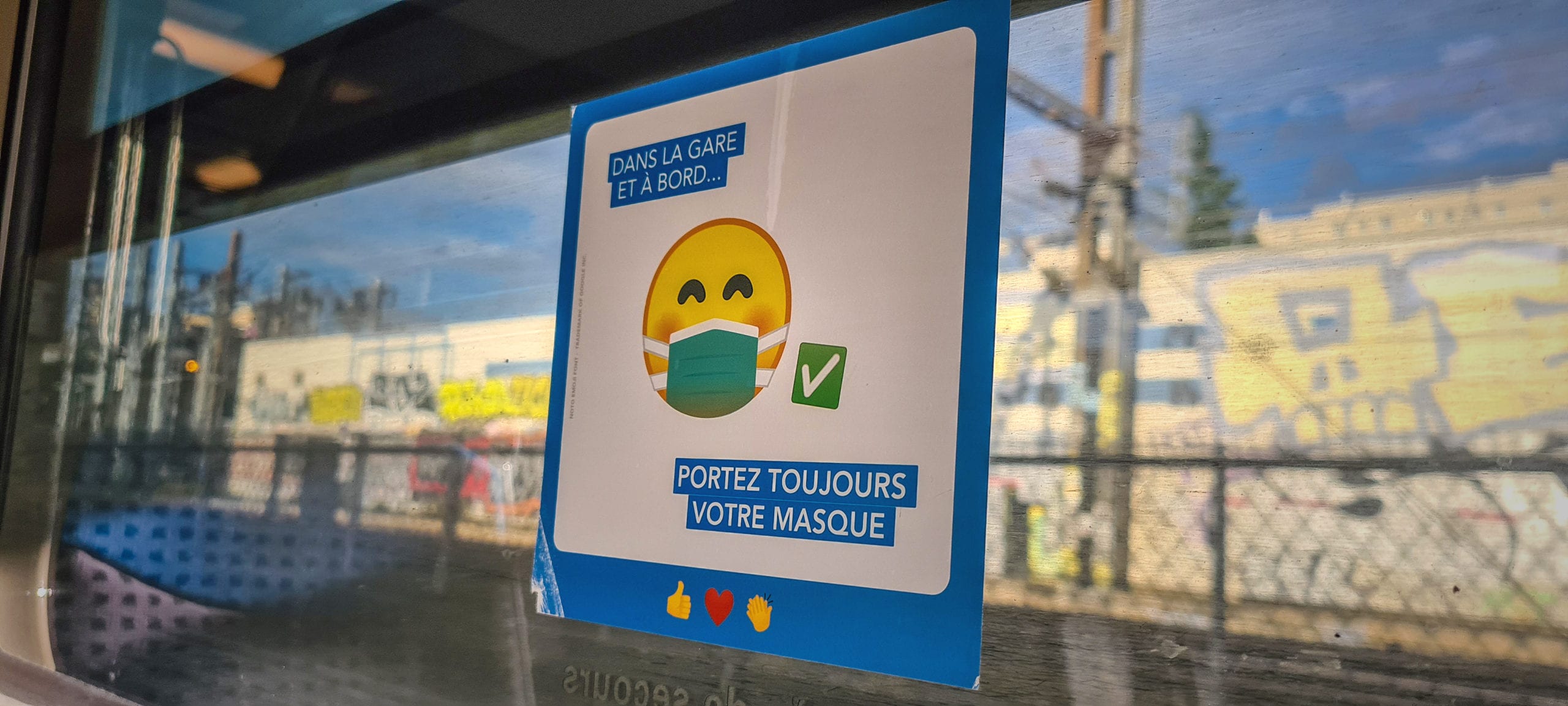 a sticker with an emoji wearing a mask telling you to wear your mask (in French) on a train window