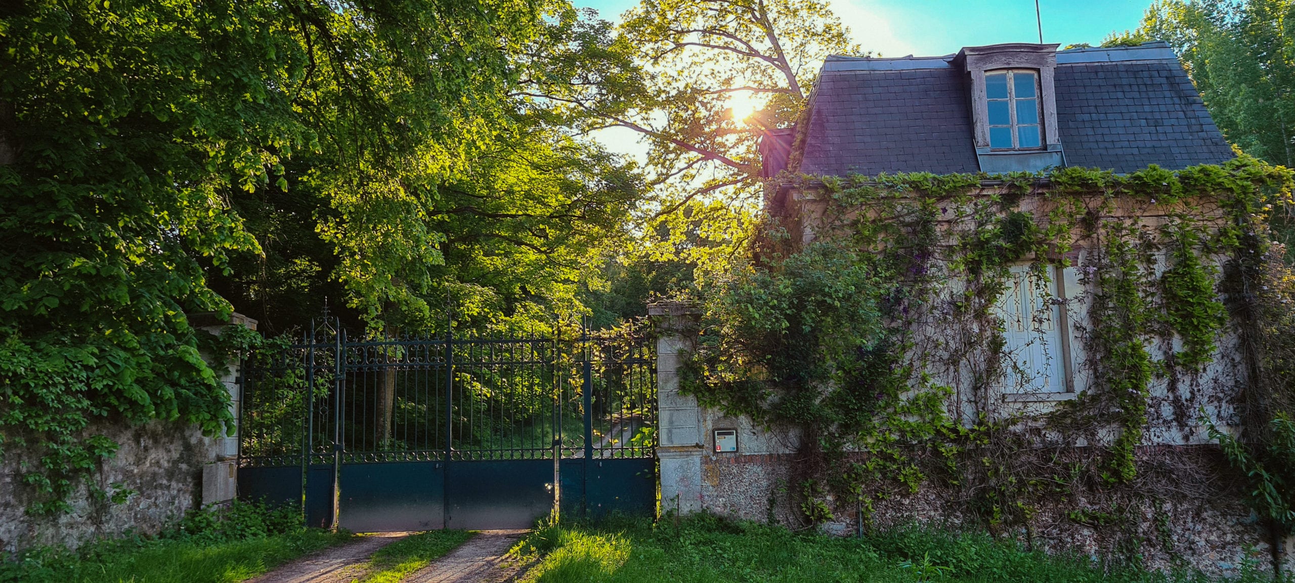 a gate and gatehouse at the end of a wooded drive