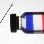 a needle and clear dose of liquid reflecting the French flag