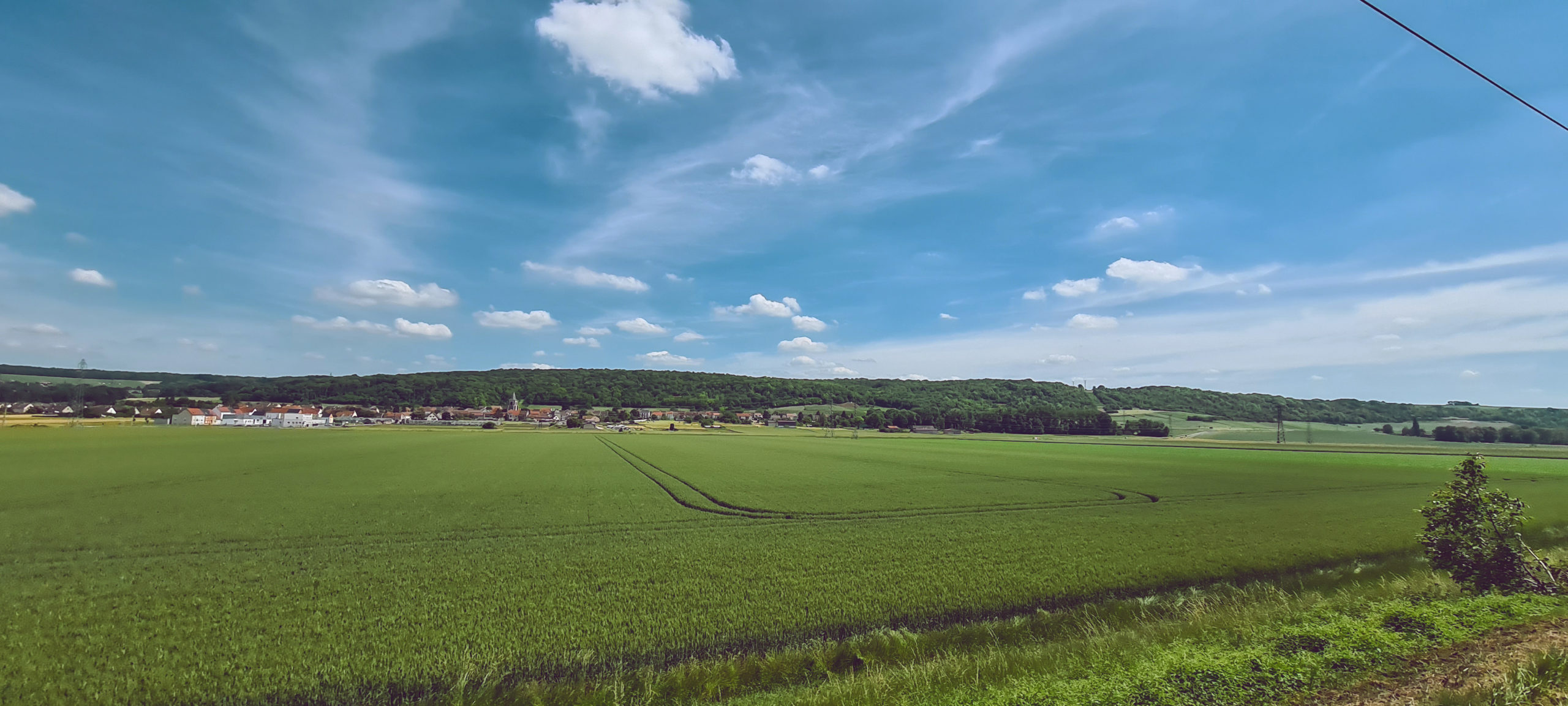 blue sky and farm land with a small village in the distance, view from a moving train window