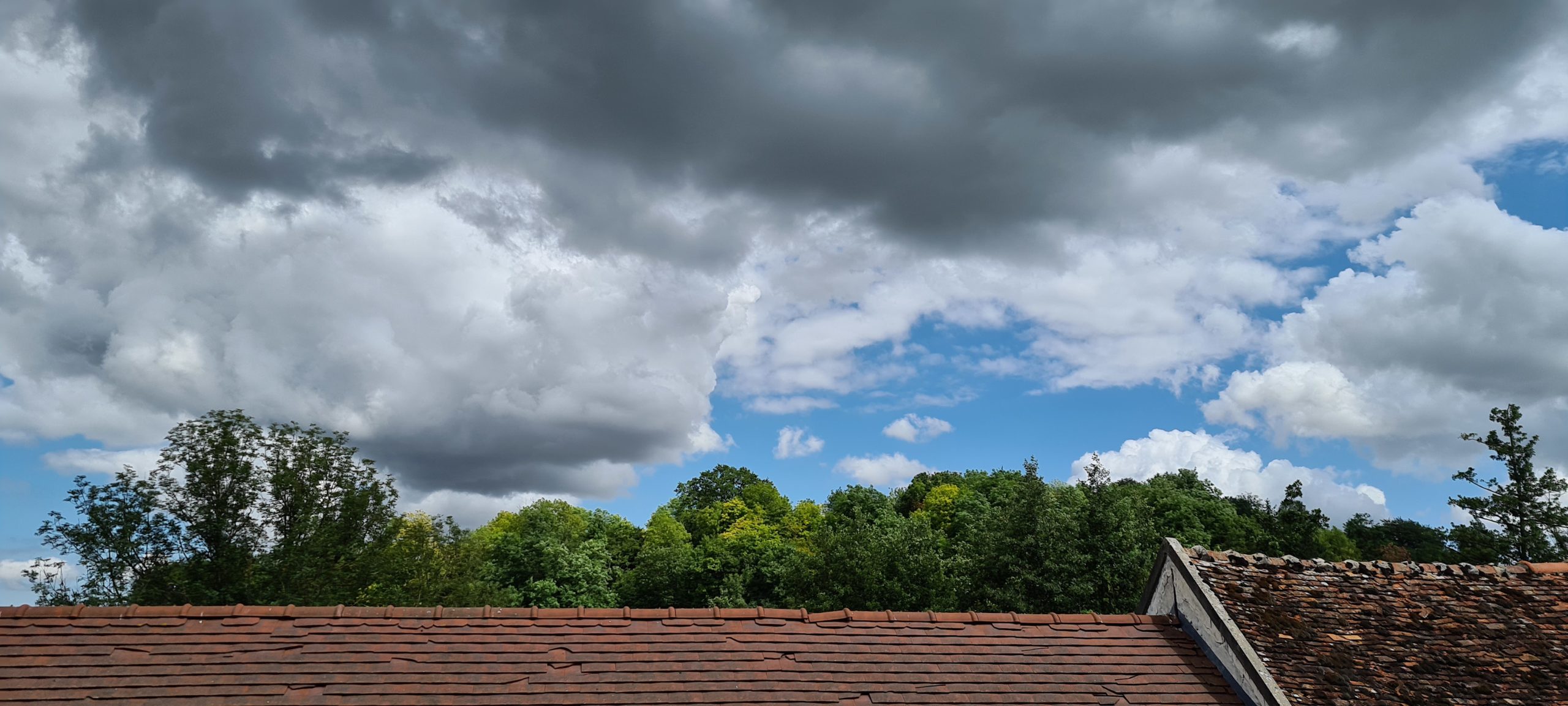 white and grey clouds over trees and a roof