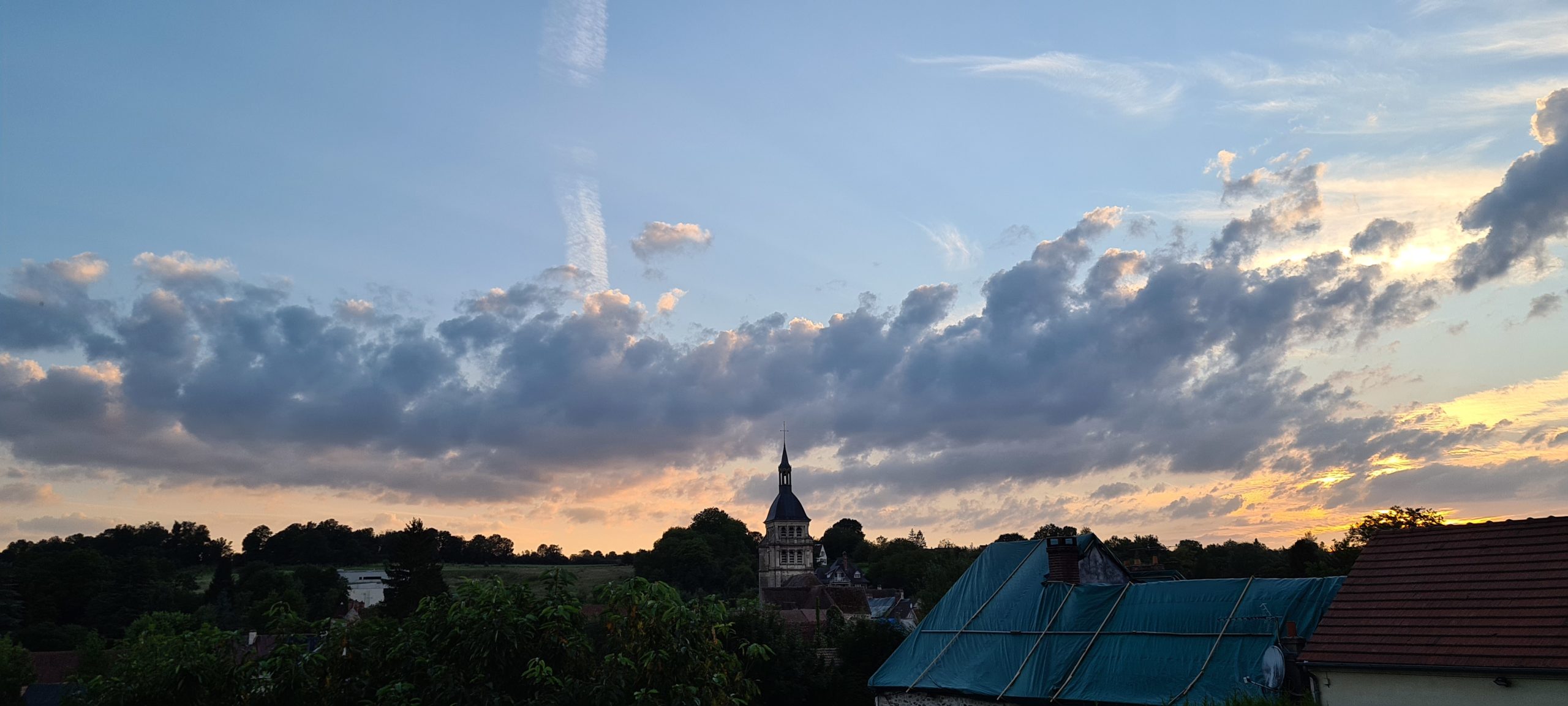 sunset behind clouds and a few buildings including a church steeple