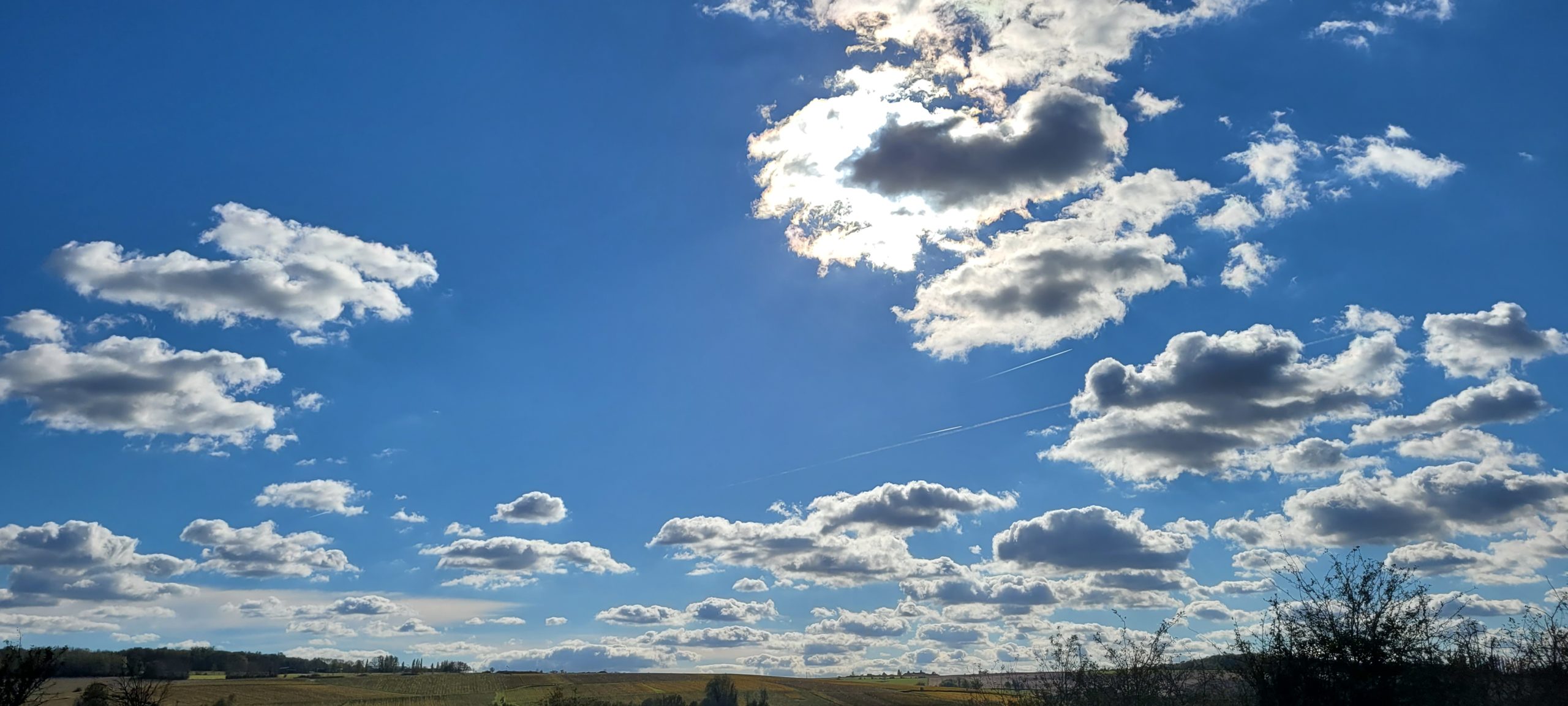 blue sky with sun behind white clouds