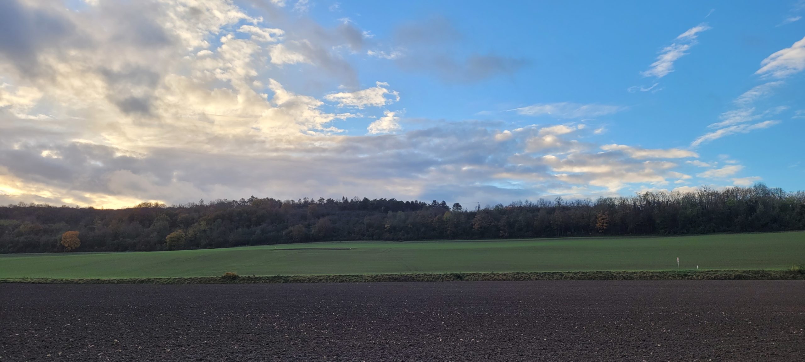 blue sky with white clouds at sunrise over farm land and hill with trees