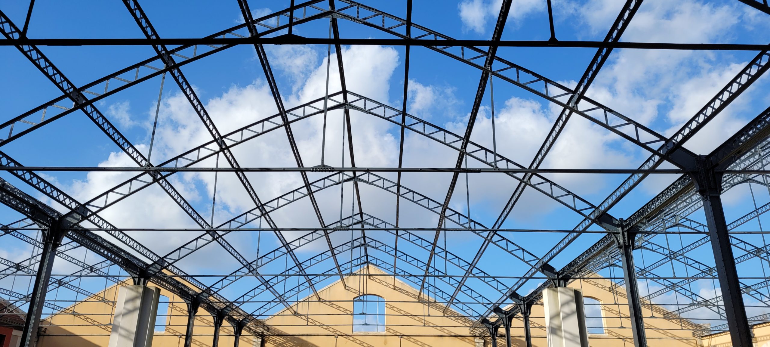 metal beams of what was a roof on a large building, blue sky with clouds seen through it