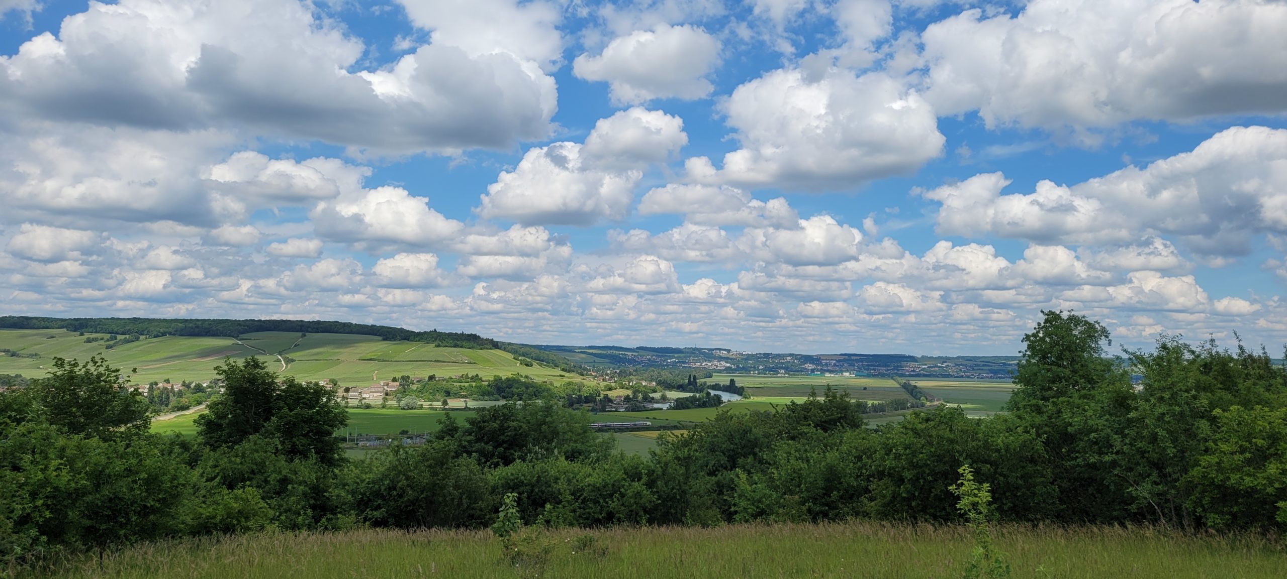 fluffly white clouds hanging low in a blue sky over green hills