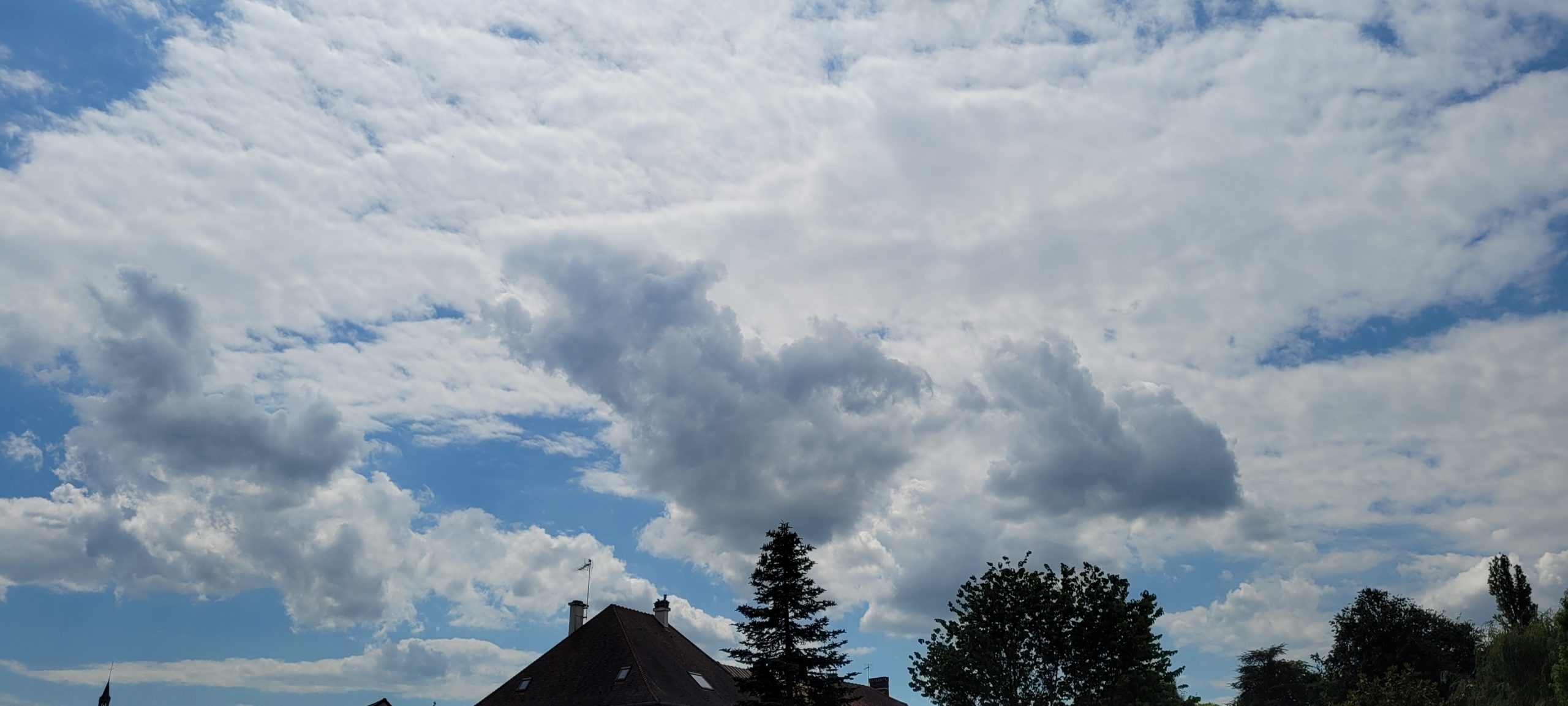 white clouds above a house and trees