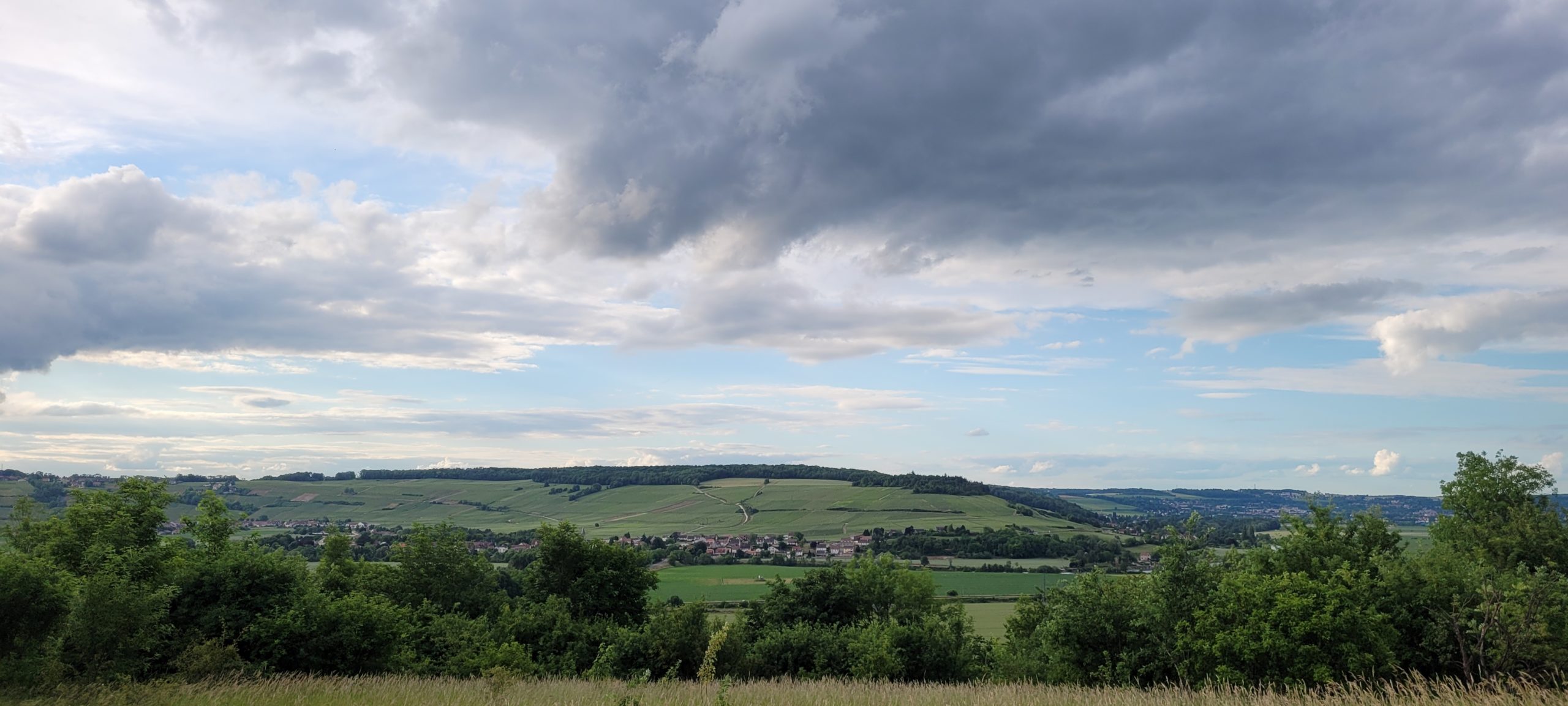 grey and white clouds in a blue sky over green hills