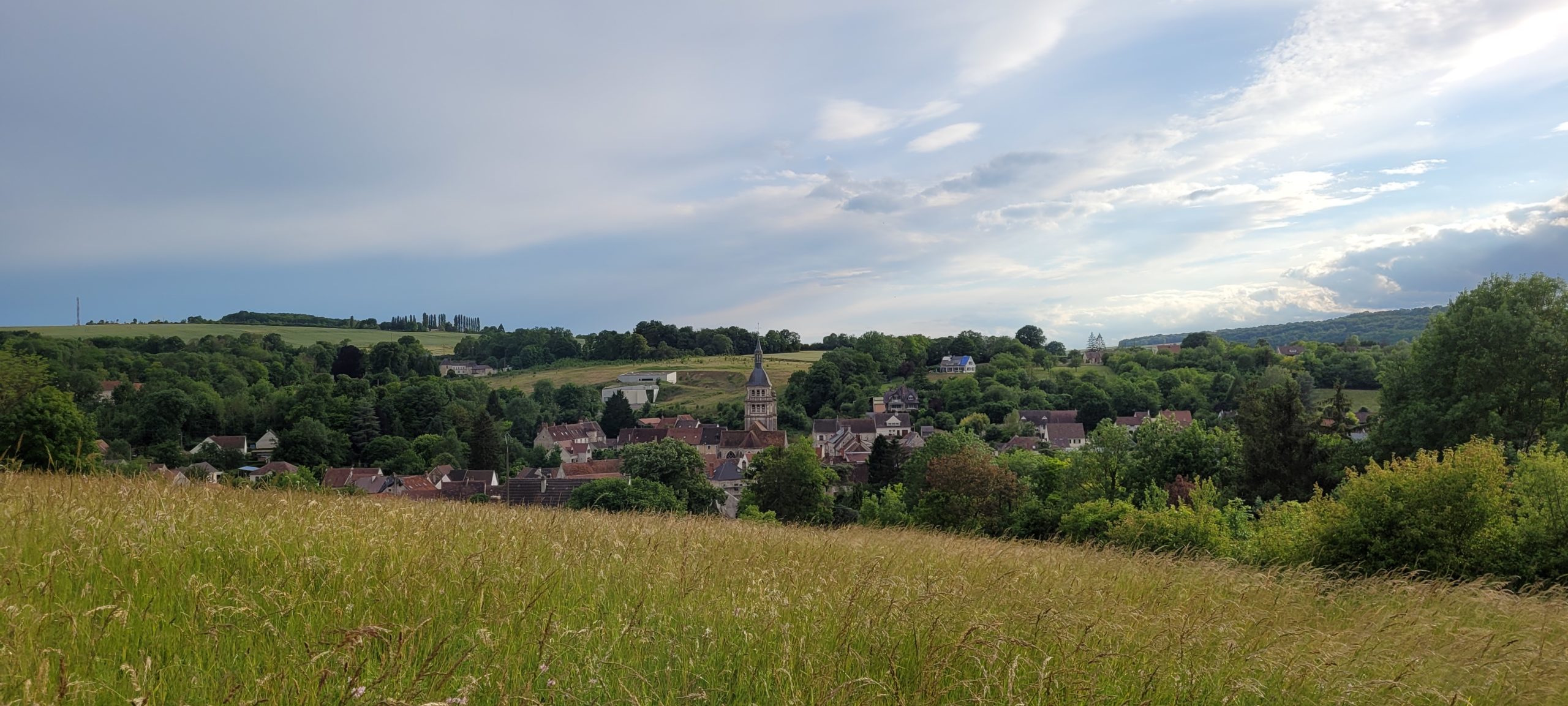 blue sky with white cloud cover over green hills and a small village