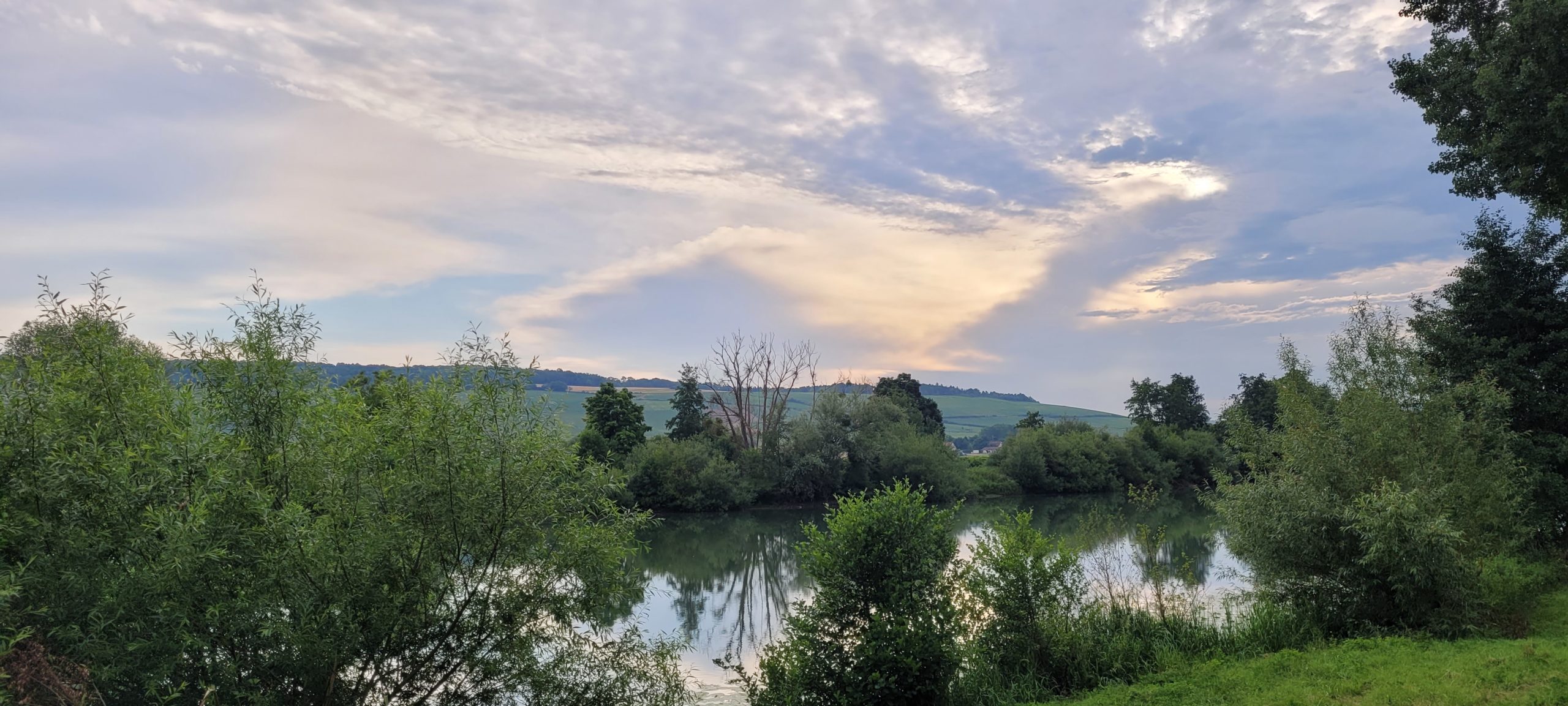 cloudy sunrise over a river lined with green trees