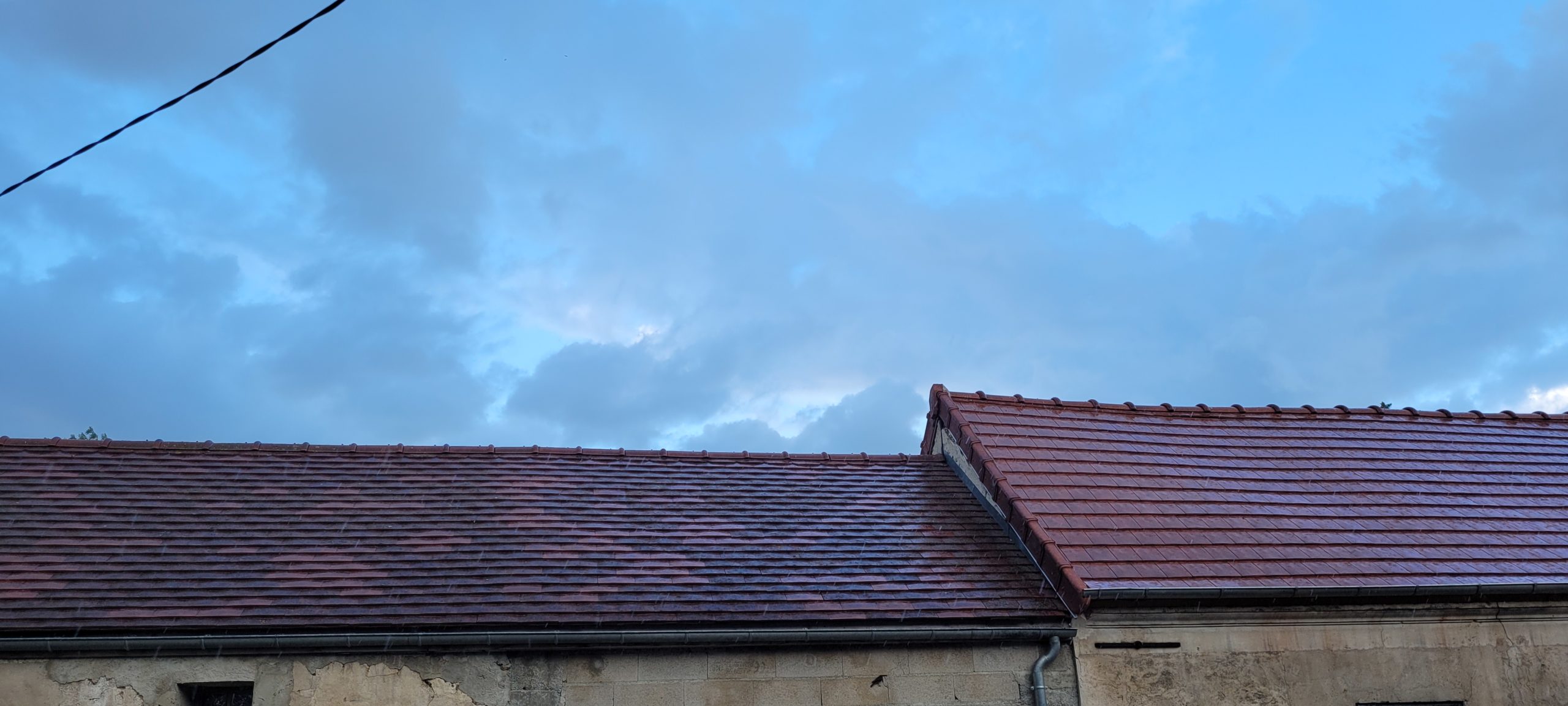 light clouds in a blue sky above roofs in light rain