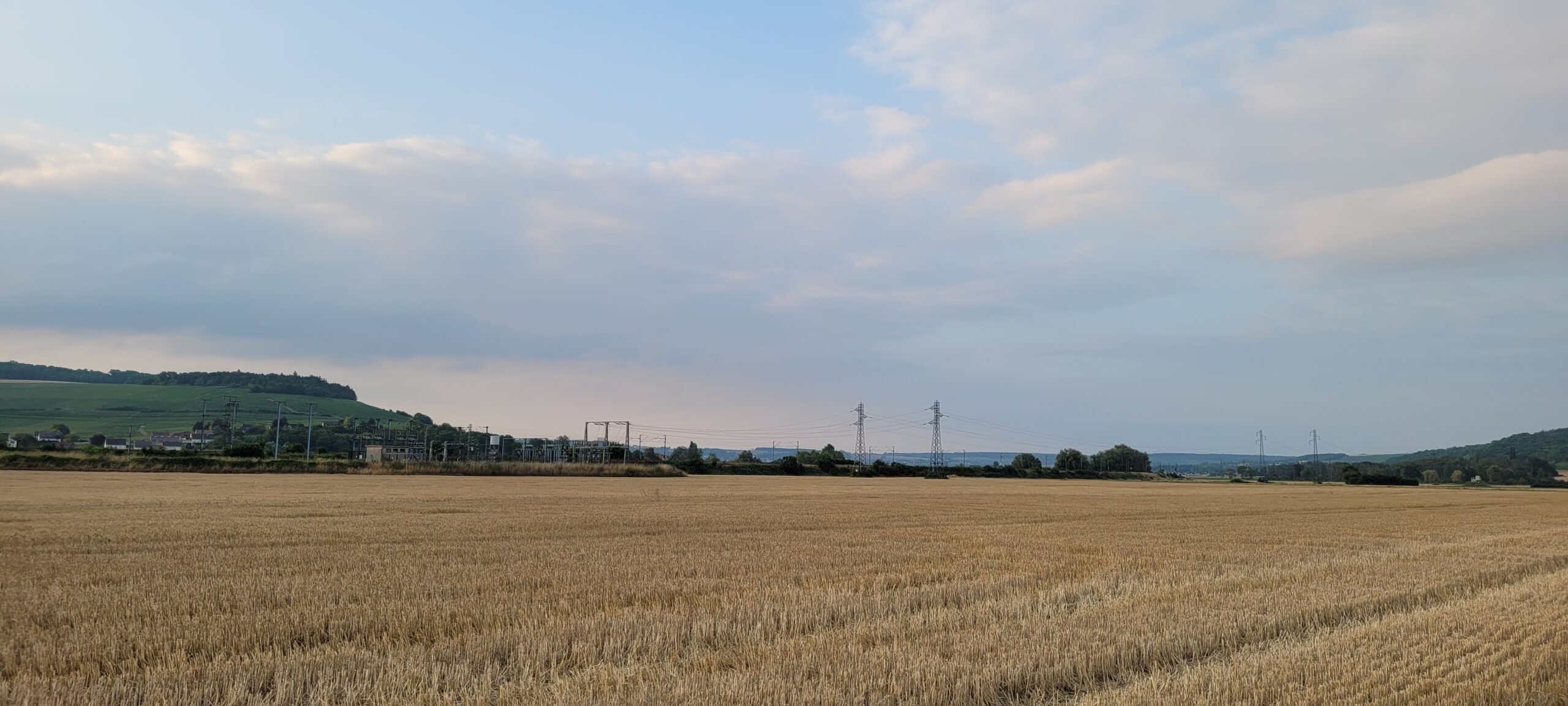 farm field below white fluffly clouds at sunrise