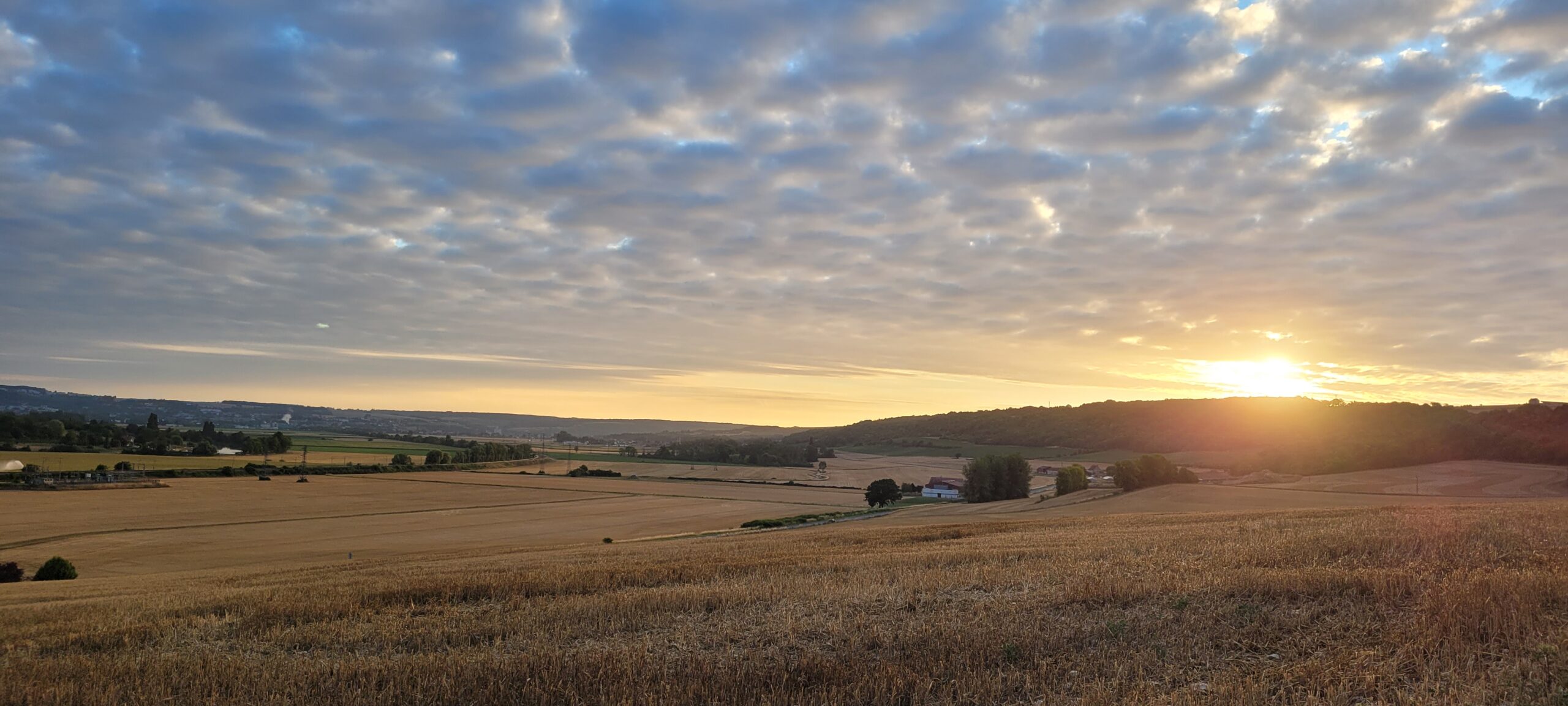 Sunrise behind a hill over farm fields