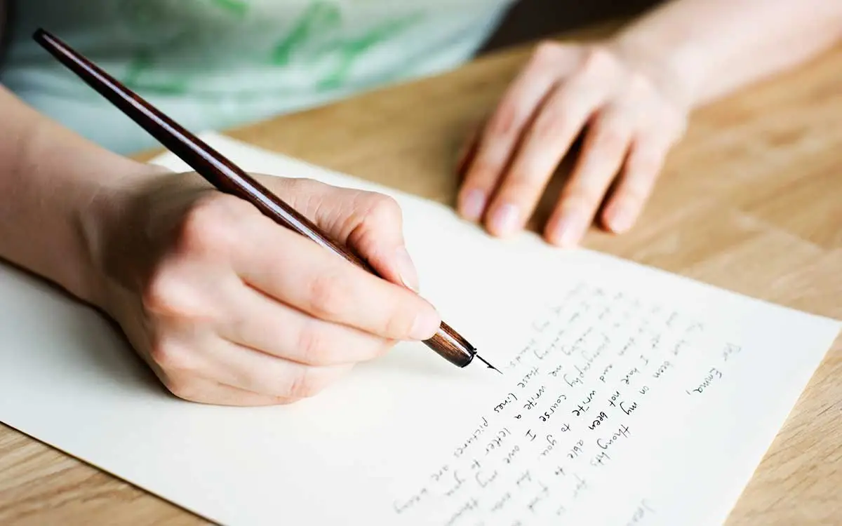 a fair skinned person holding a pen and writing on white paper