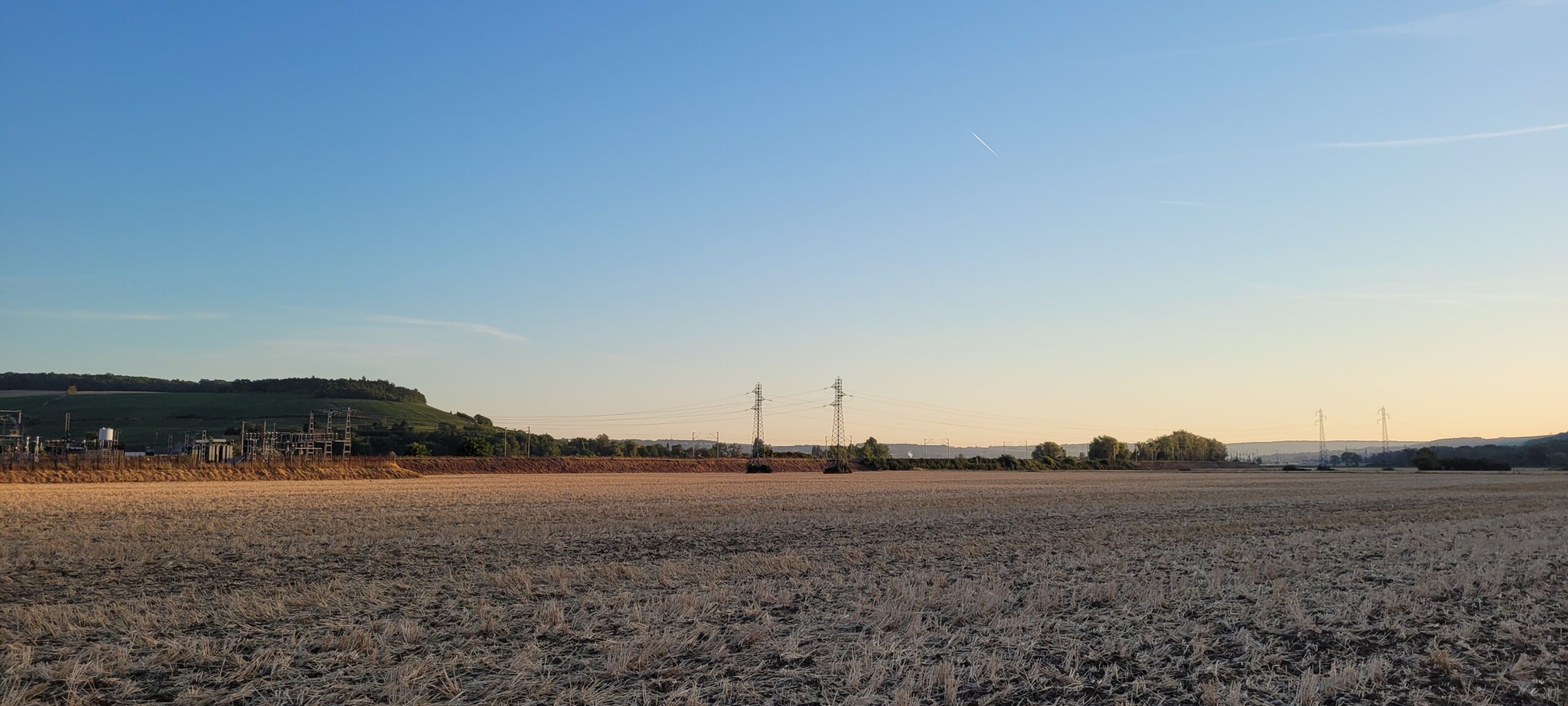 sunrise colors in a clear sky over plowed field, power lines in the background