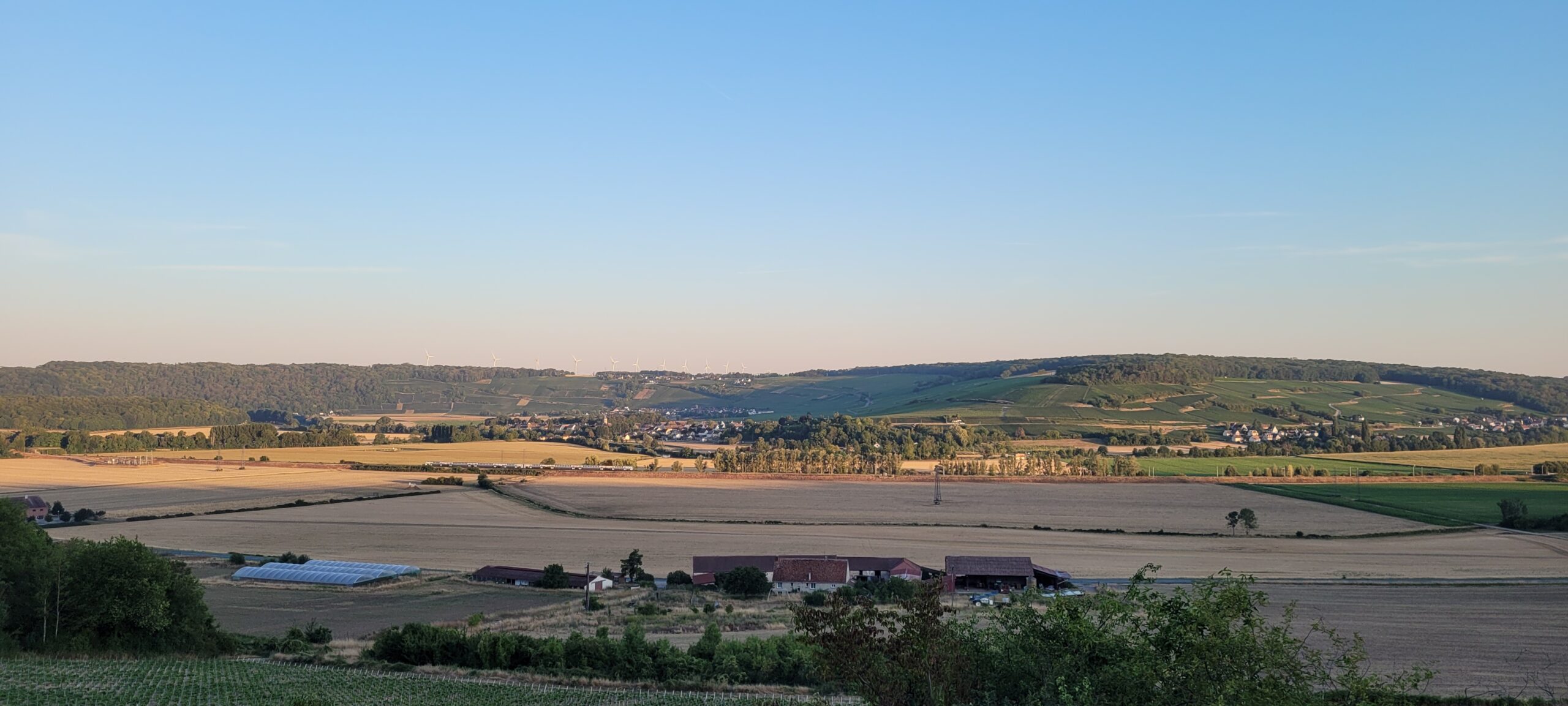 a valley with farm buildings and train tracks at sunrise, clear sky