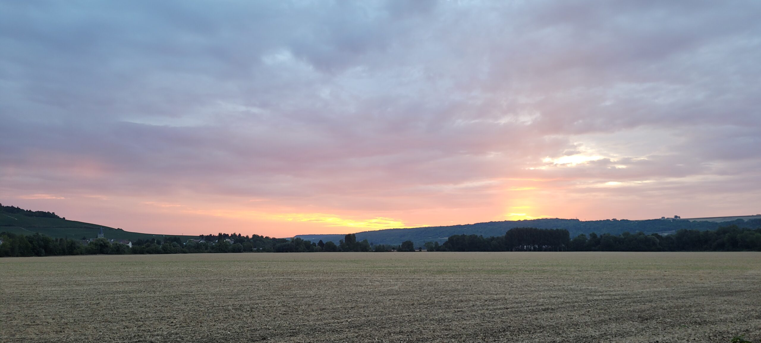 sunrise in a cloudy sky, orange, pink, and blue/grey over farm fields