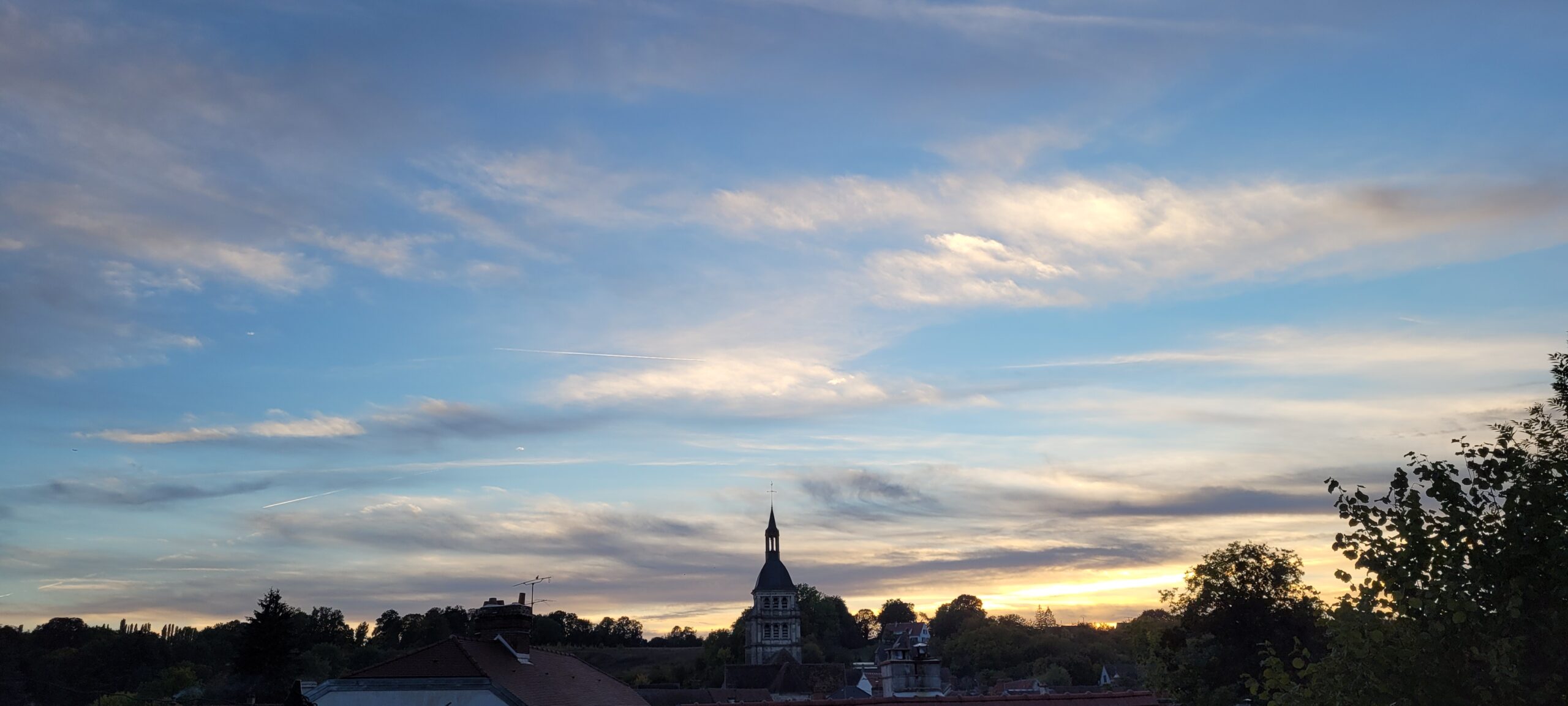 sunset sky of blue and yellows with a church steeple and village silhouetted