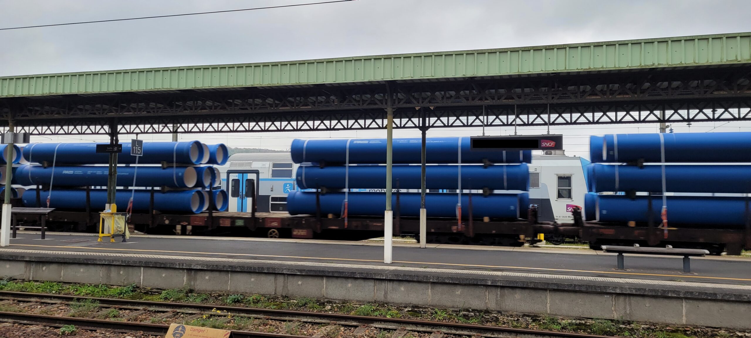 large blue tubes being transported on a train driving through a station