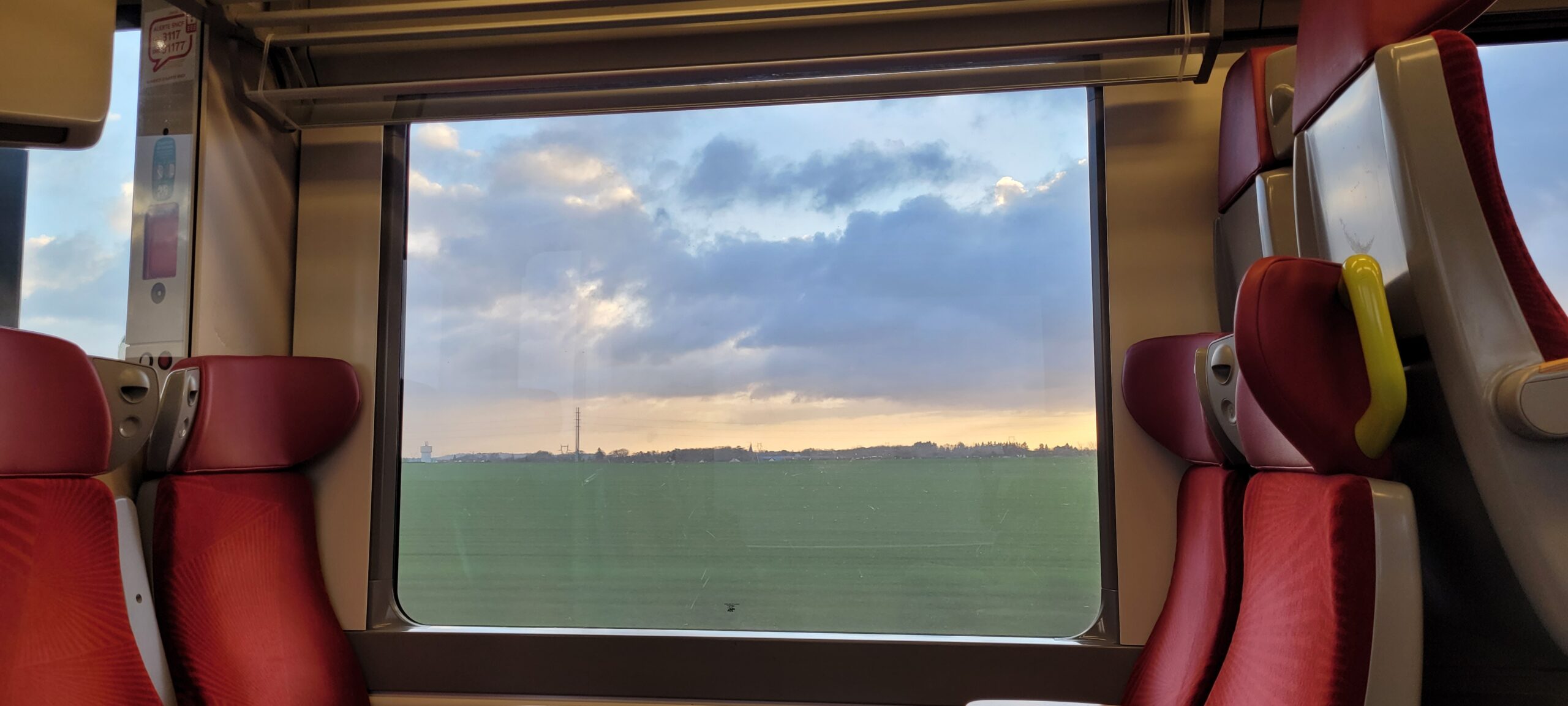 sunrise colors in a cloudy sky outside a large train window