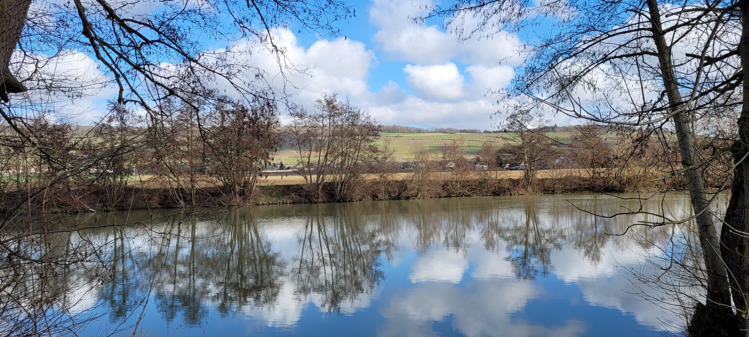 blue sky with puffy white clouds over a river reflecting